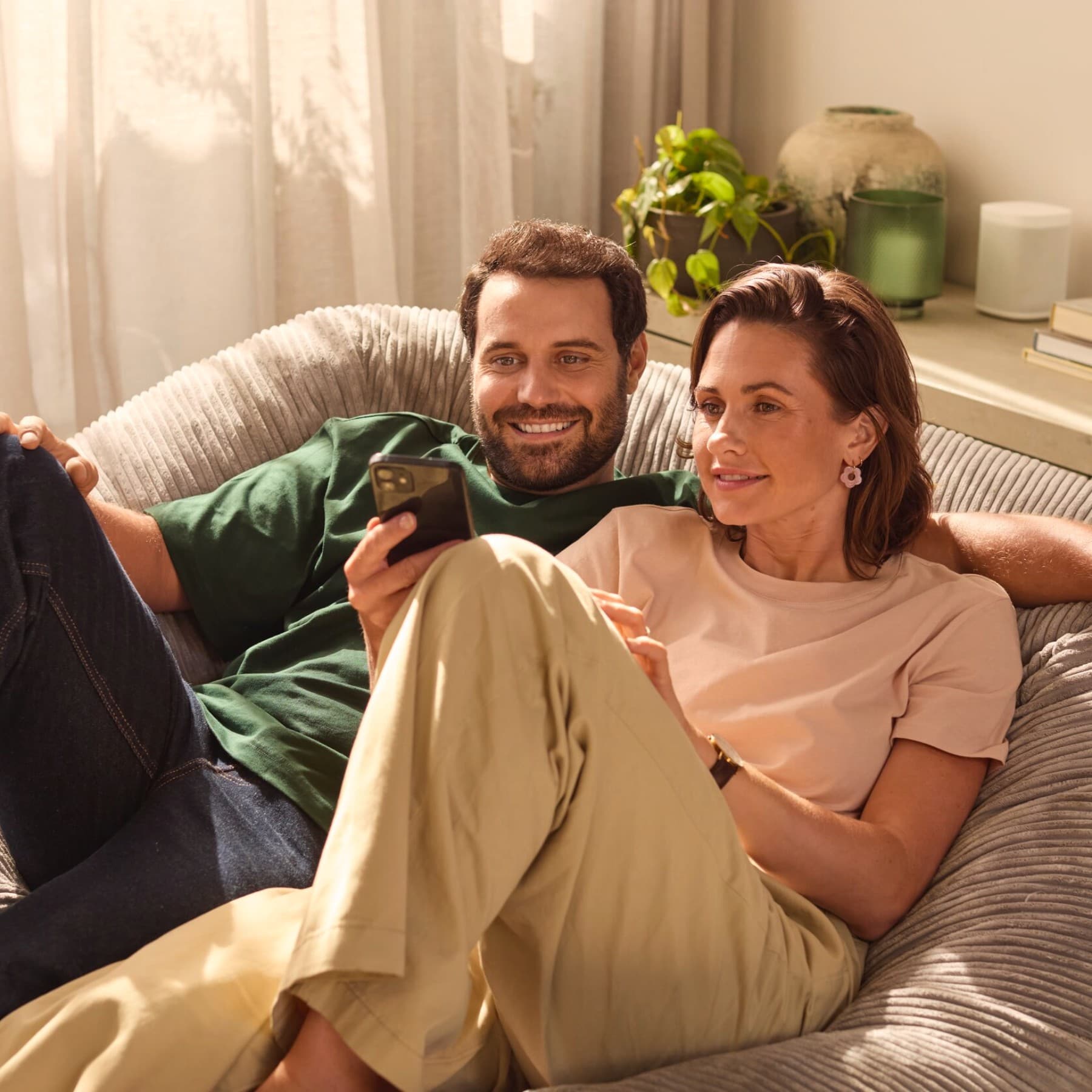 Пар седи на софа гледајќи во паметен телефон