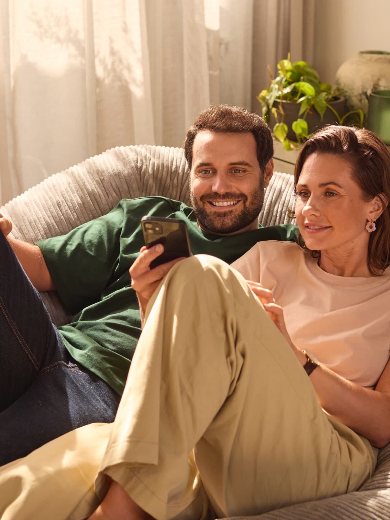 Пар седи на софа гледајќи во паметен телефон