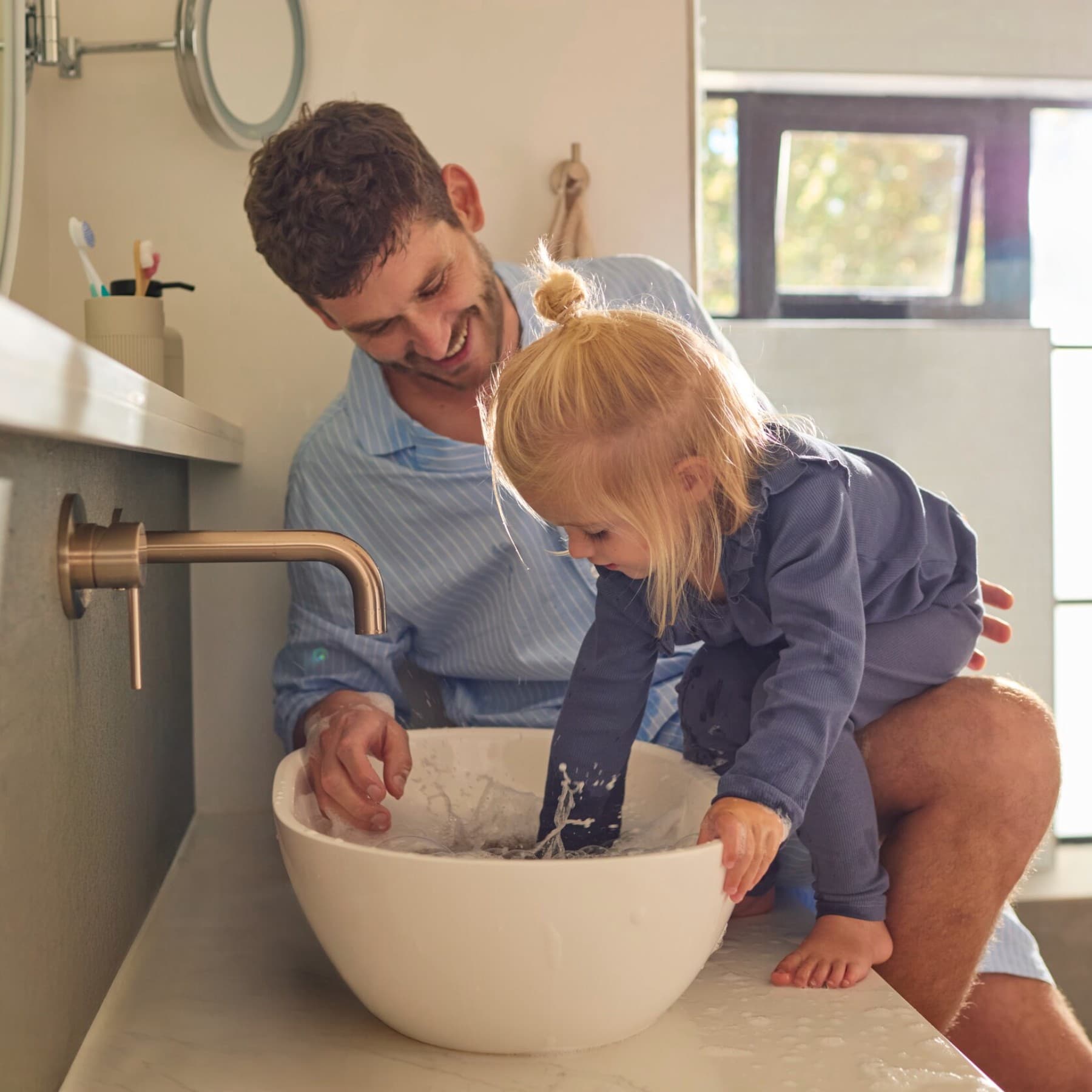 Татко и ќерка си играат со водата во мијалникот