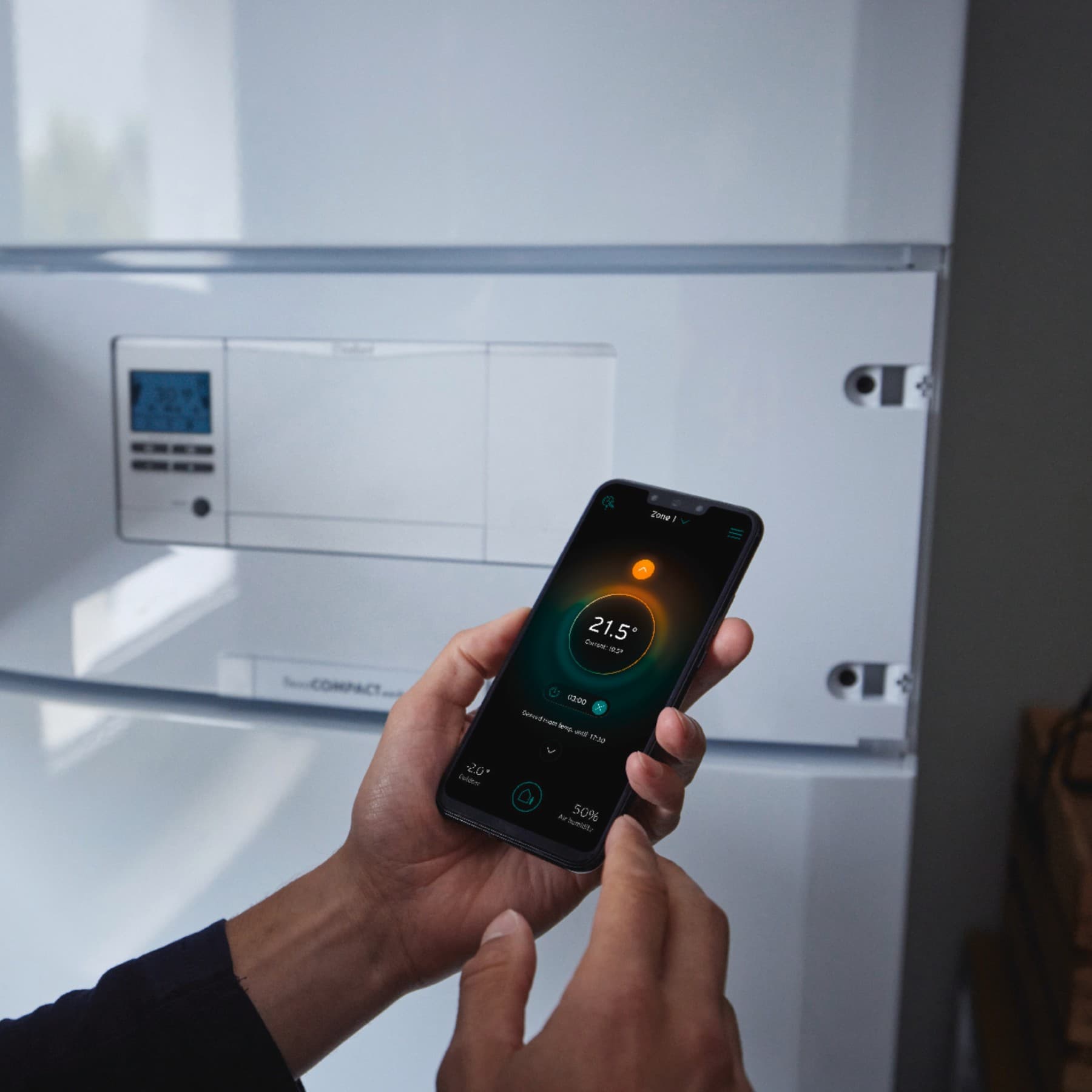 Човек држи мобилен телефон пред бојлер