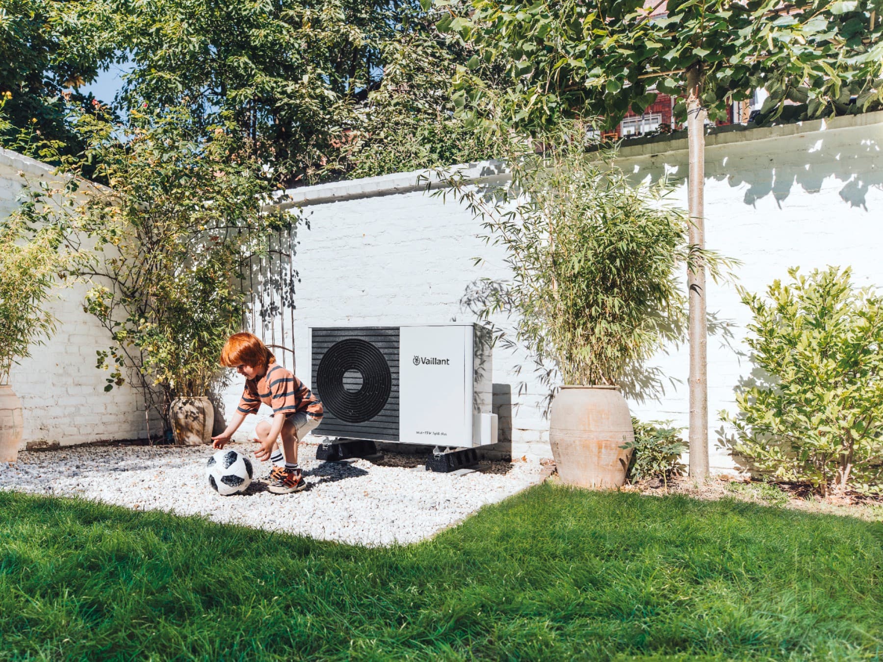 Дете игра фудбал во градината пред топлинска пумпа