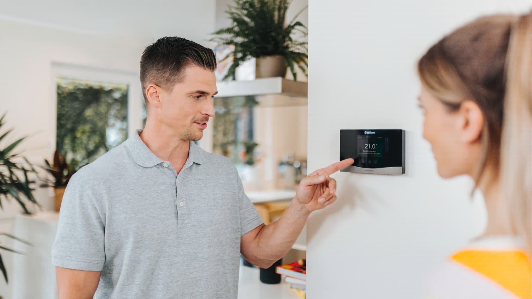 Човек е во преден план со раката на регулатор за греење монтиран на син ѕид