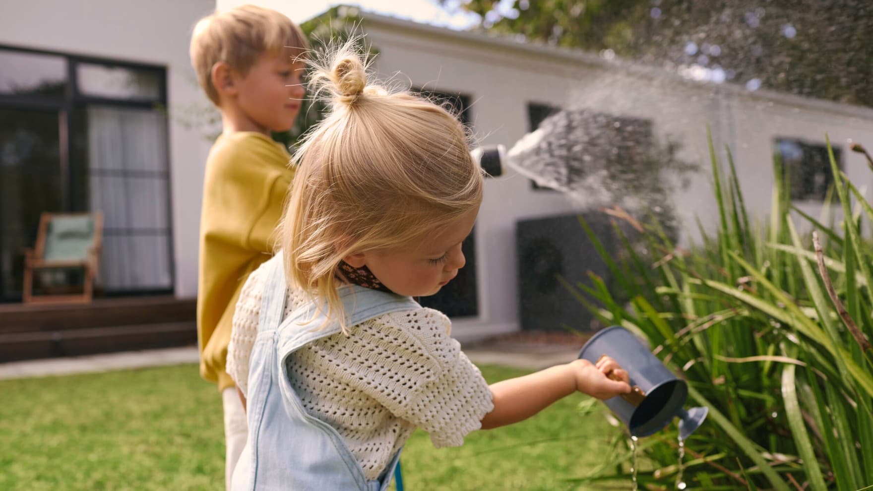 Деца полеваат растенија во градинка со топлинска пумпа во позадина