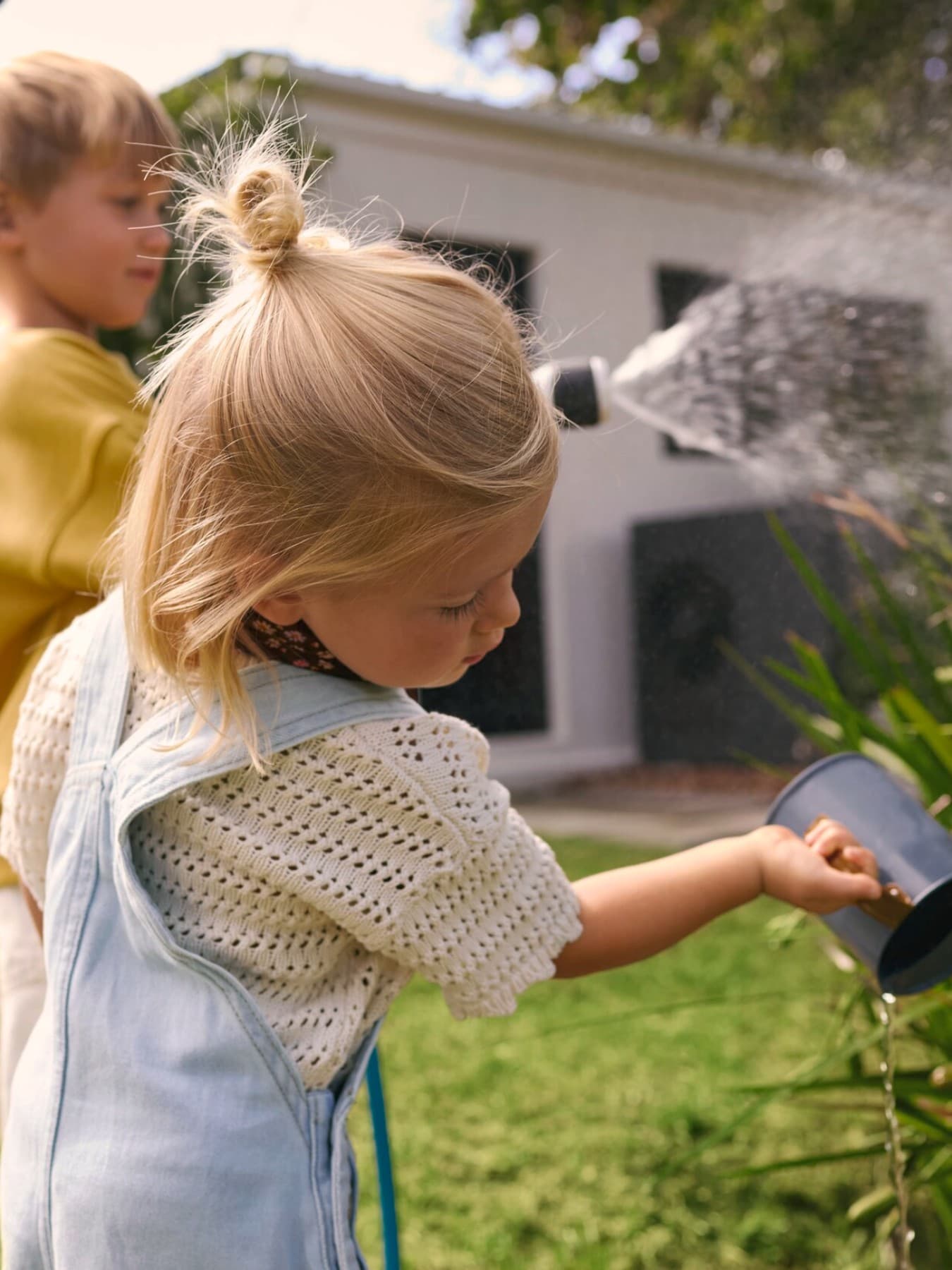 Деца полеваат растенија во градинка со топлинска пумпа во позадина