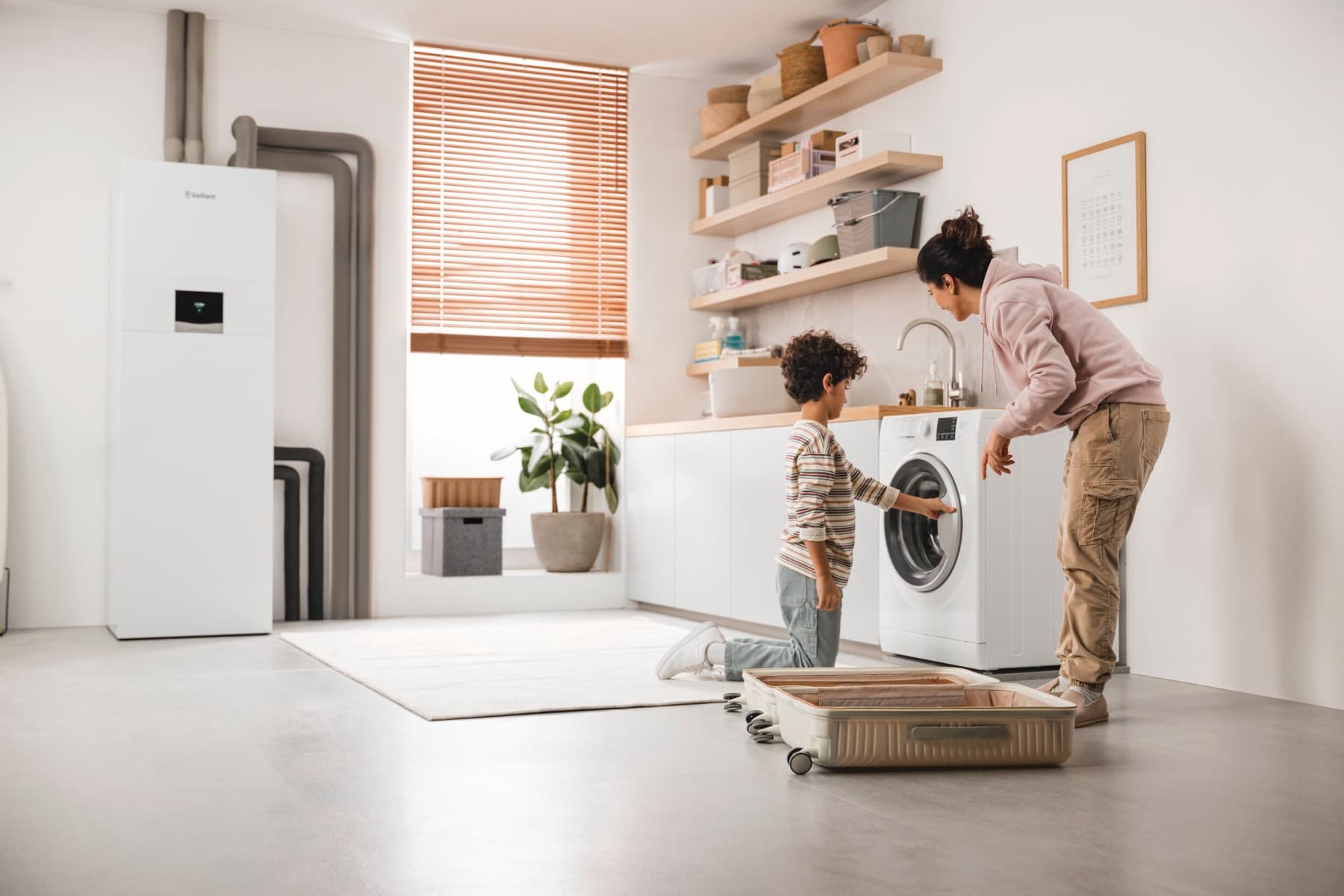 Мајка и син ја проверуваат машината за перење а во позадина има топлинска пумпа од земја